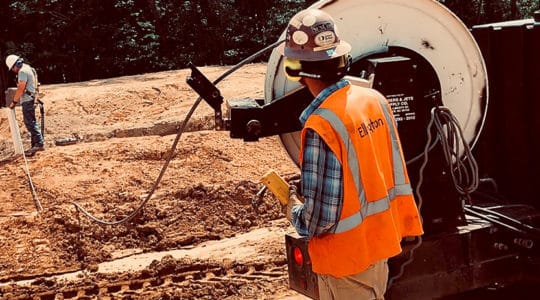 worker watches as coworker feeds hose into tube