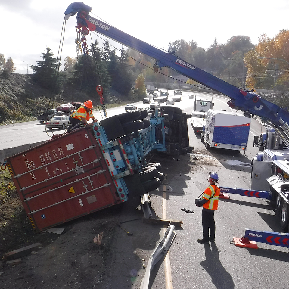 Towing and recovery crew prepare to lift rolled semi-tractor trailer.