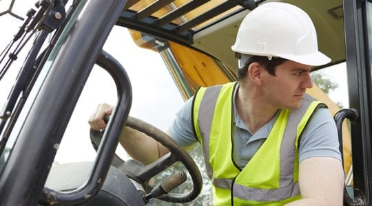 Worker in hard hat and safety vest driving heavy equipment