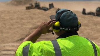 man looking out at worksite wearing cap and noise cancelling headset