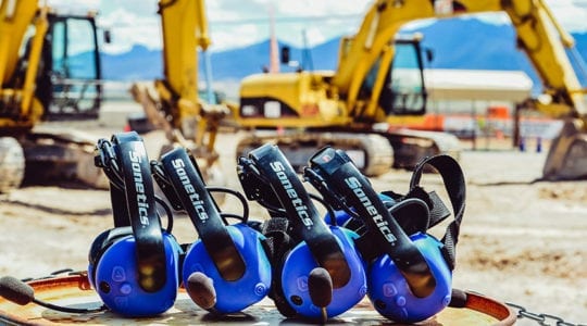 Four Sonetics wireless headsets on the ground in front of construction equipment